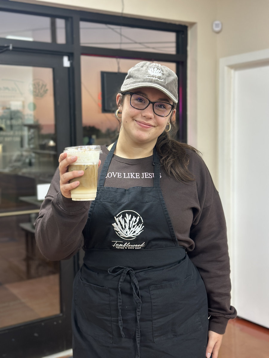 A smiling barista holding an iced coffee drink.